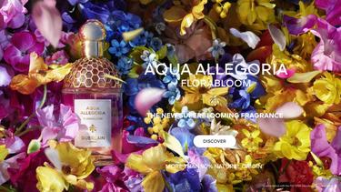 The image is an advertisement for the "Aqua Allegoria Forte" perfume by Guerlain. It features a golden perfume bottle amidst a backdrop of multicolored roses with water-like reflections, emphasizing luxury and natural ingredients.