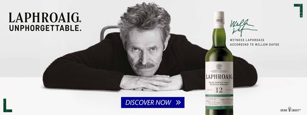 Laphroaig single malt Scotch whisky ad featuring a 12-year-old bottle, Willem Dafoe’s signature, black-and-white portrait, slogan “Laphroaig. Unphorgettable.” and “Discover now” button on a white and green background.