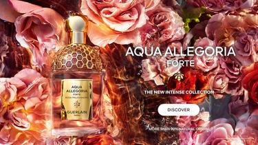 The image is an advertisement for the "Aqua Allegoria Forte" perfume by Guerlain. It features a golden perfume bottle amidst a backdrop of multicolored roses with water-like reflections, emphasizing luxury and natural ingredients. The ad invites viewers t
